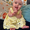 baby, child, infant, smiling, happy, clapping, sitting, portrait, indoors, couch, pillows, yellow_dress, headband, flower, polka_dots, stuffed_animal, blanket, barefoot, cozy, closeup