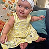 baby, child, infant, portrait, smiling, sitting, dress, yellow_dress, headband, flower, couch, cushions, indoor, home, playful, barefoot, eyes, face, photography, adorable