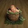 newborn, baby, sleeping, wooden_bucket, green_fabric, headband, infant, floor, cozy, portrait, soft_lighting, rustic, cute, resting, child, indoors, peaceful, decor, texture, photography