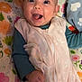 baby, smiling, happy, infant, blanket, floral_pattern, sleeping_bag, blue_sleeves, hand, face, cute, child, indoors, portrait, lying_down, cheerful, cozy, expression, toddler, bright_eyes