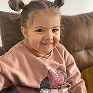 April a rejoint le concours — aidez-le/la à gagner de superbes lots ! child, girl, smiling, hair_buns, minnie_mouse, sweatshirt, pink_clothing, couch, indoor, portrait, cute, happy, person, young_child, casual, seated, cozy, home, fashion, face