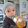 Enzo participe au concours pour gagner de l'argent avec cette photo : toddler, child, bottle, hat, knit_hat, drink, indoor, table, face, eyes, hand, sweater, home, play_kitchen, photograph, curious, young_child, cozy, casual, portrait