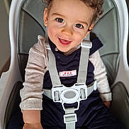 Ezio a rejoint le concours — aidez-le/la à gagner de superbes lots ! toddler, child, high_chair, curly_hair, smiling, happy, indoor, straps, clothing, person, face, seated, cute, baby, infant, playful, expression, skin, eyes, hand