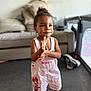 toddler, child, smiling, clapping, overalls, minnie_mouse, pink, sandals, indoors, living_room, sofa, shoes, hair_bun, cute, happy, person, floor, playpen, earrings, portrait