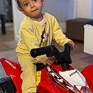 Lunna a rejoint le concours — aidez-le/la à gagner de superbes lots ! toddler, child, toy, atv, red, indoor, yellow_clothing, floor, furniture, person, vehicle, play, young_child, expression, handlebars, casual, home, footwear, curly_hair, portrait