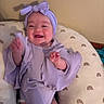 baby, child, smiling, headband, purple_clothing, cushion, rainbow_pattern, indoor, happy, person, infant, seated, cute, apparel, headwear, wall, comfort, joy, portrait, young_child
