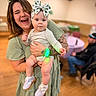Fiona is registered to the contest to win money with this photo: baby, background, blur, child, dress, floor, green, happy, headband, holding, indoor, light, people, person, shamrock, smiling, sneakers, tattoo, woman, wristband
