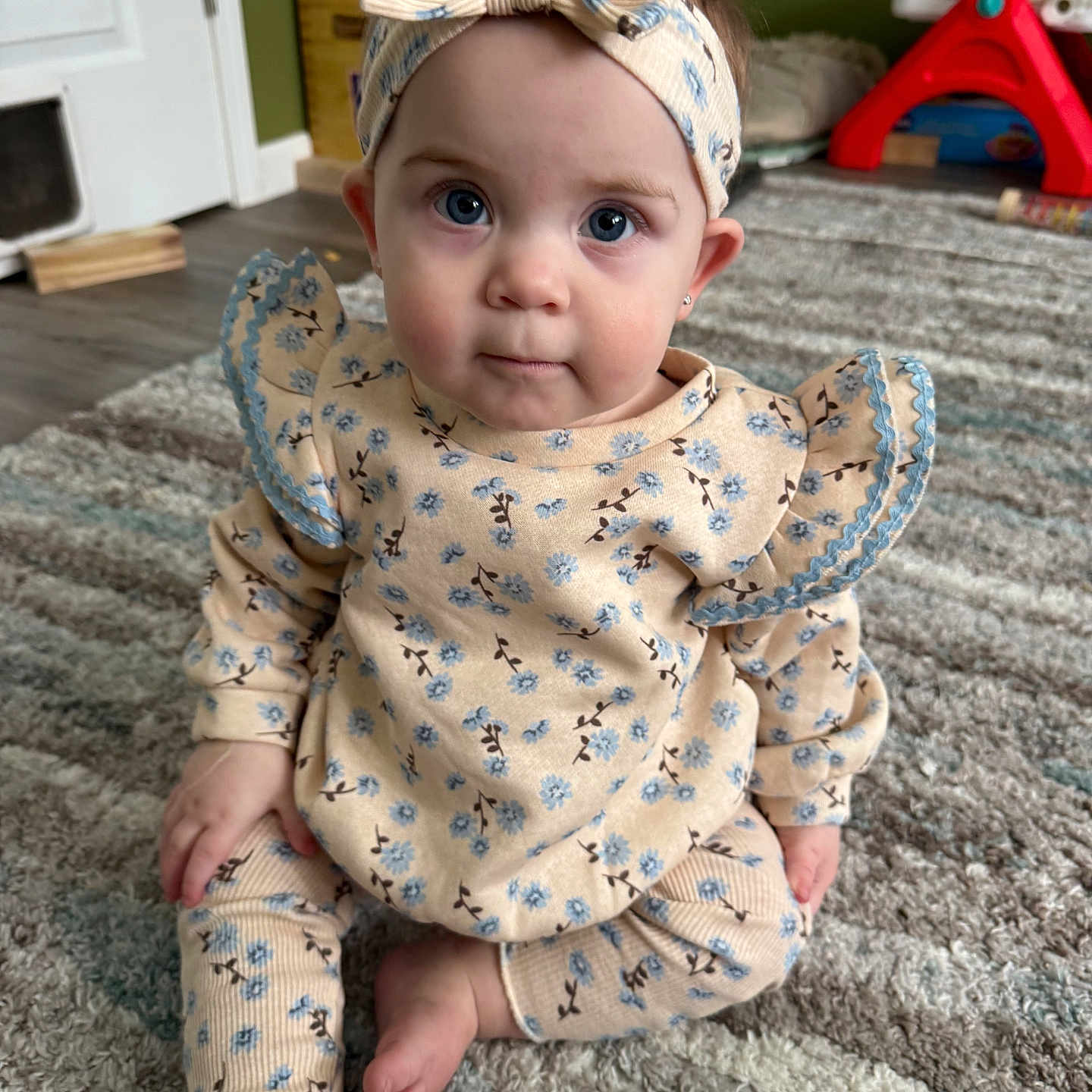 Fiona joined the competition — help win amazing prizes! baby, bow, carpet, child, clothing, cute, expression, eyes, face, floor, floral_clothing, foot, hand, headband, indoor, infant, portrait, room, sitting, toy