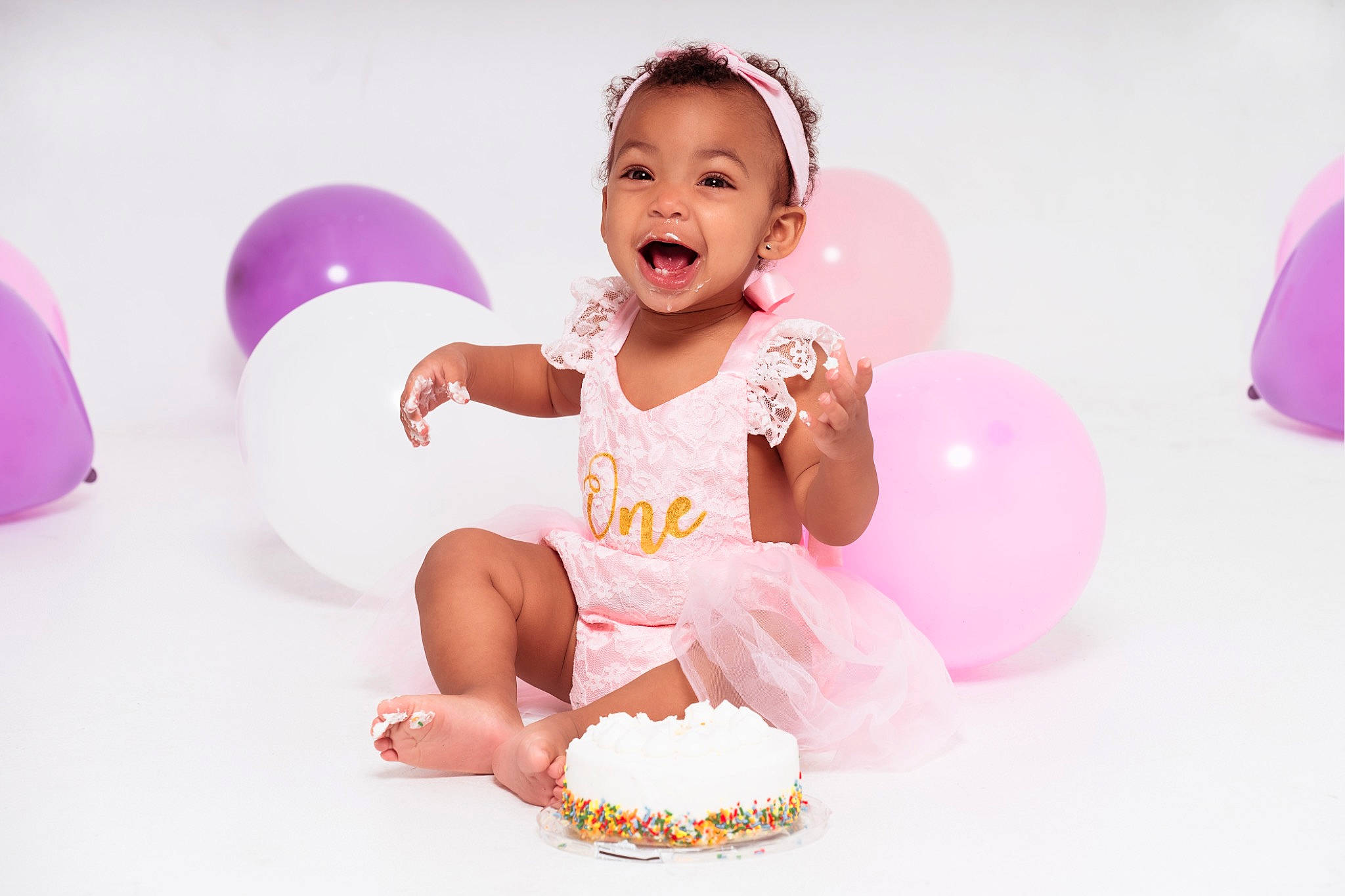 Leilahni is registered to the contest to win money with this photo: baby, baby_toddler_clothing, balloon, child, dress, event, facial_expression, finger, flash_photography, fun, happy, icing, ingredient, magenta, party_supply, person, pink, smile, sugar_cake, sweetness