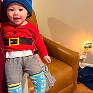 Lindsey joined the competition — help win amazing prizes! baby, child, hat, colorful_hat, red_shirt, striped_pants, blue_socks, horse_socks, smiling, indoor, living_room, leather_chair, wood_floor, night_light, pineapple_light, person_holding, happy, cute, cozy, portrait