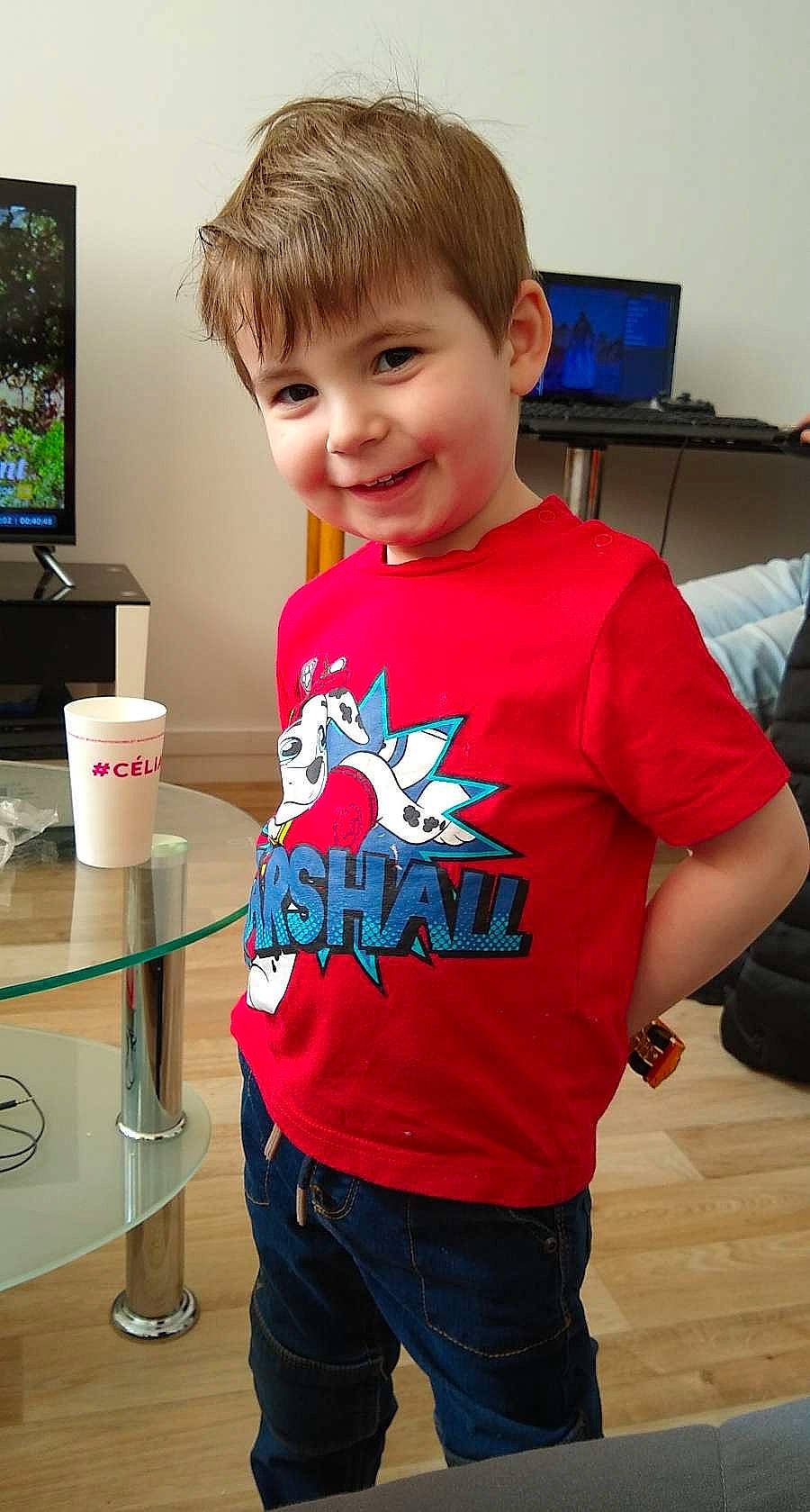 Théo participe au concours pour gagner de l'argent avec cette photo : bag, child, display_device, drinkware, electric_blue, flooring, fun, hairstyle, happy, joint, joy, luggage_and_bags, person, shoulder, sleeve, smile, standing, t_shirt, table, television