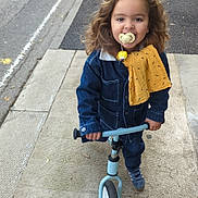 Isaac participe au concours pour gagner de l'argent avec cette photo : child, toddler, balance_bike, sidewalk, denim_jacket, pacifier, yellow_cloth, curly_hair, outdoor, street, footwear, casual_clothing, happy, person, urban, play, toy, young_child, smiling, daytime