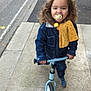 child, toddler, balance_bike, sidewalk, denim_jacket, pacifier, yellow_cloth, curly_hair, outdoor, street, footwear, casual_clothing, happy, person, urban, play, toy, young_child, smiling, daytime