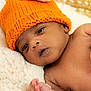 baby, infant, hat, orange_hat, knit_hat, newborn, face, skin, hand, blanket, soft_texture, lying_down, closeup, curious, indoors, warm_colors, cute, portrait, baby_boy, resting