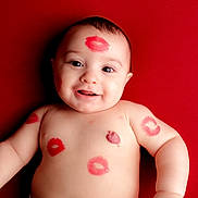 Liam is registered to the contest to win money with this photo: baby, infant, smiling, face, kiss_mark, red_background, skin, arm, chest, tongue, happy, cute, portrait, child, lipstick, lying_down, playful, person, expression, closeup