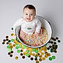 Liam joined the competition — help win amazing prizes! baby, bowl, cereal, colorful, coins, gold, green, black, smiling, sitting, white_background, infant, cute, playful, festive, food, candy, happy, indoors, child
