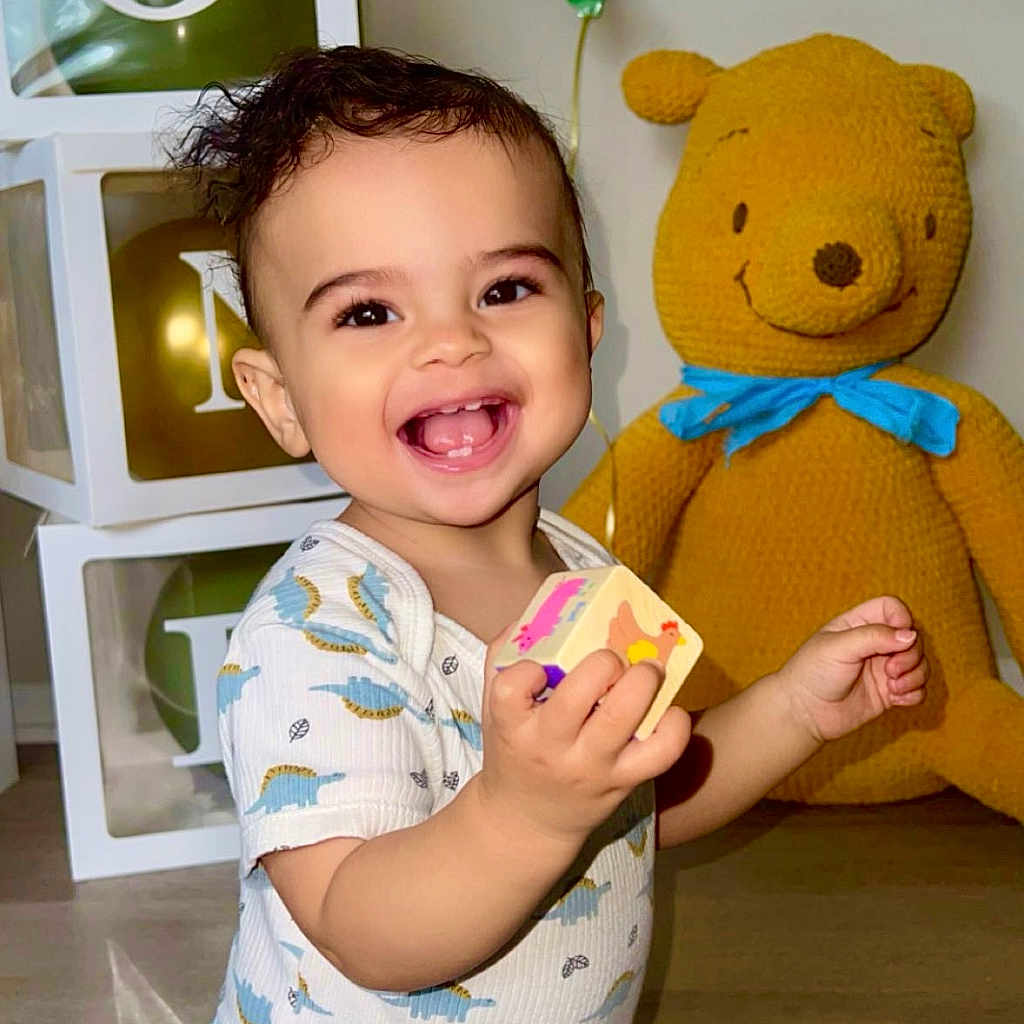 Mikah is registered to the contest to win money with this photo: baby, balloon, block, blue_clothing, child, cute, denim_pants, face, floor, green_balloon, happy, home, indoor, joy, knitted_bear, person, playful, smiling, toddler, toy