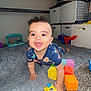 Mikah is registered to the contest to win money with this photo: baby, child, crawling, toy_train, colorful_blocks, rug, curly_hair, smiling, indoor, storage_bins, lamp, floor, playtime, happy, person, carpet, toy, infant, room, childhood