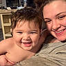 child, toddler, woman, smile, happy, indoor, family, person, hair, face, expression, blanket, casual_clothing, holding, joy, home, cozy, light, portrait, together