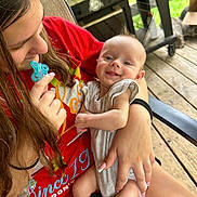 Ayson joined the competition — help win amazing prizes! baby, child, woman, smile, pacifier, red_shirt, outdoor, wooden_deck, grill, chair, holding, happy, person, casual, summer, cute, relaxed, family, portrait, skin