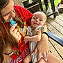 baby, child, woman, smile, pacifier, red_shirt, outdoor, wooden_deck, grill, chair, holding, happy, person, casual, summer, cute, relaxed, family, portrait, skin