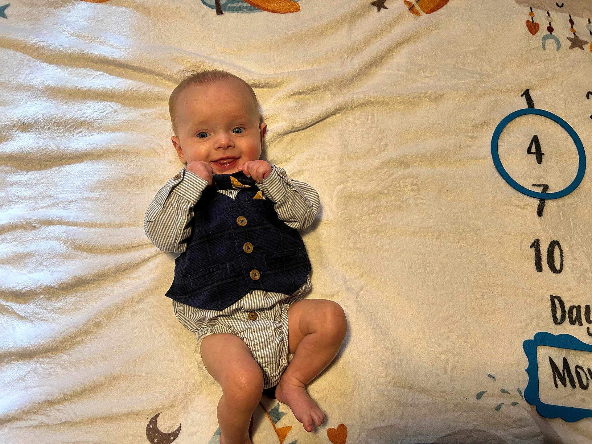 Ayson is registered to the contest to win money with this photo: baby, infant, child, vest, bow_tie, striped_clothing, blanket, numbers, moon, smiling, lying_down, playful, cute, happy, indoors, soft_texture, portrait, young_child, baby_clothes, face