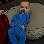 baby, pacifier, blue_onesie, pillow, cushion, infant, person, face, indoors, bed, blanket, soft_lighting, expression, portrait, child, sleepwear, comfort, relaxed, young, cute