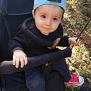 Lucas participe au concours pour gagner de l'argent avec cette photo : child, toddler, stroller, baseball_cap, hat, outdoors, forest, trees, leaves, stick, red_sneakers, hand, eyes, smile, jacket, pants, grass, portrait, adorable, sitting