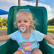 Ellie joined the competition — help win amazing prizes! child, toddler, pacifier, slide, playground, outdoor, blue_sky, summer_clothing, bow, grass, park, happy, smiling, casual, daylight, shorts, tshirt, play, young_child, fun