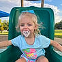 child, toddler, pacifier, slide, playground, outdoor, blue_sky, summer_clothing, bow, grass, park, happy, smiling, casual, daylight, shorts, tshirt, play, young_child, fun