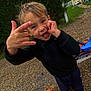 Iago a rejoint le concours — aidez-le/la à gagner de superbes lots ! child, boy, smiling, hand_gesture, outdoor, tricycle, orange_wheel, black_sweater, playful, happy, grass, gravel, building, doorway, person, fun, casual_clothing, daylight, young_child, nature