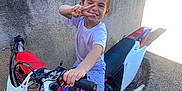 Iago a rejoint le concours — aidez-le/la à gagner de superbes lots ! barefoot, boy, casual_clothing, child, concrete_wall, daylight, dirt_bike, gravel, greenery, happy, motorcycle, outdoor, peace_sign, playful, posing, smiling, summer, sunny, vehicle, young