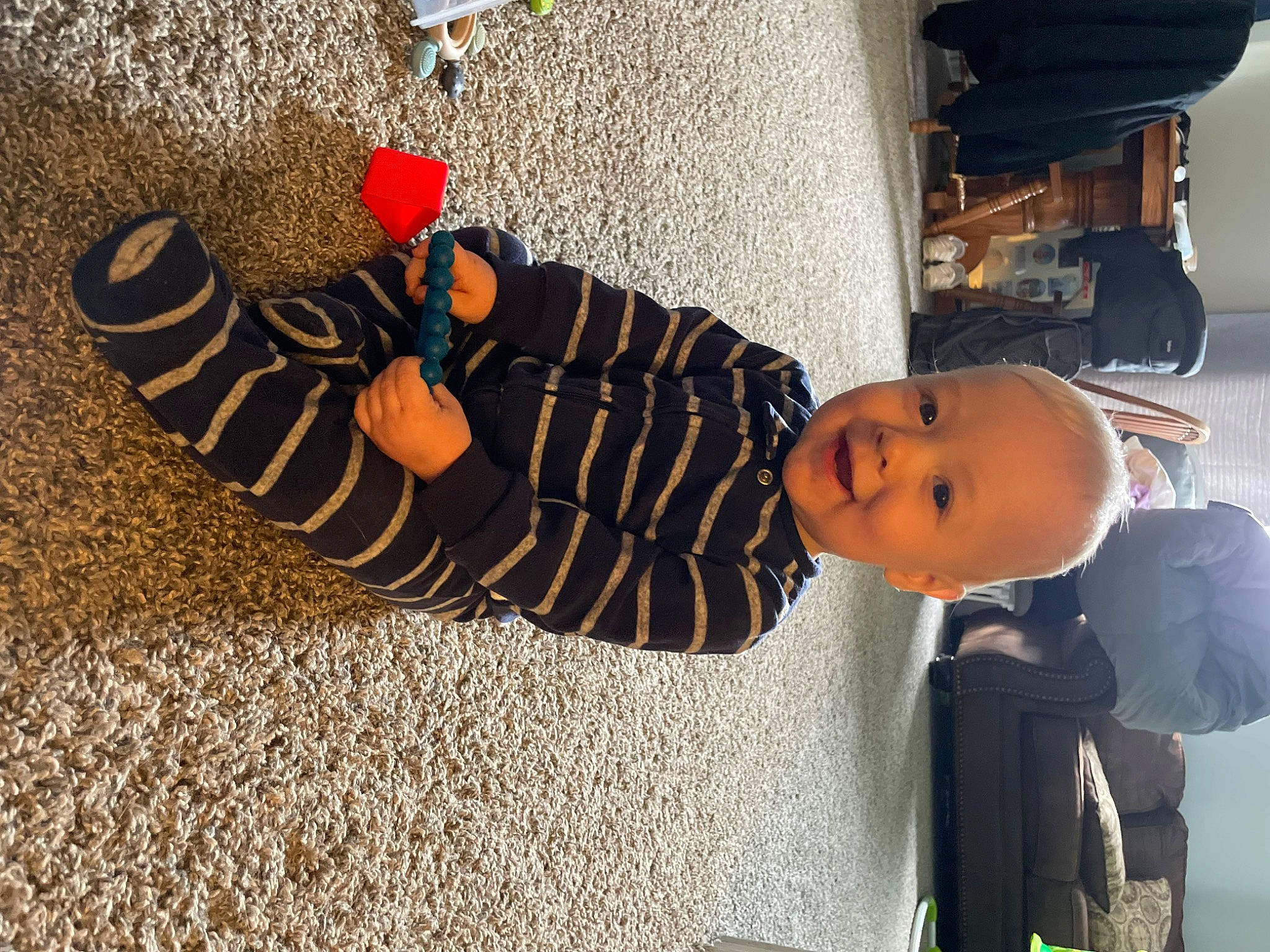 Liam is registered to the contest to win money with this photo: asphalt, baby, child, cool, flooring, foot, fun, hat, human_leg, joy, person, plant, road_surface, shadow, sitting, smile, tints_and_shades, tire, toddler, tree