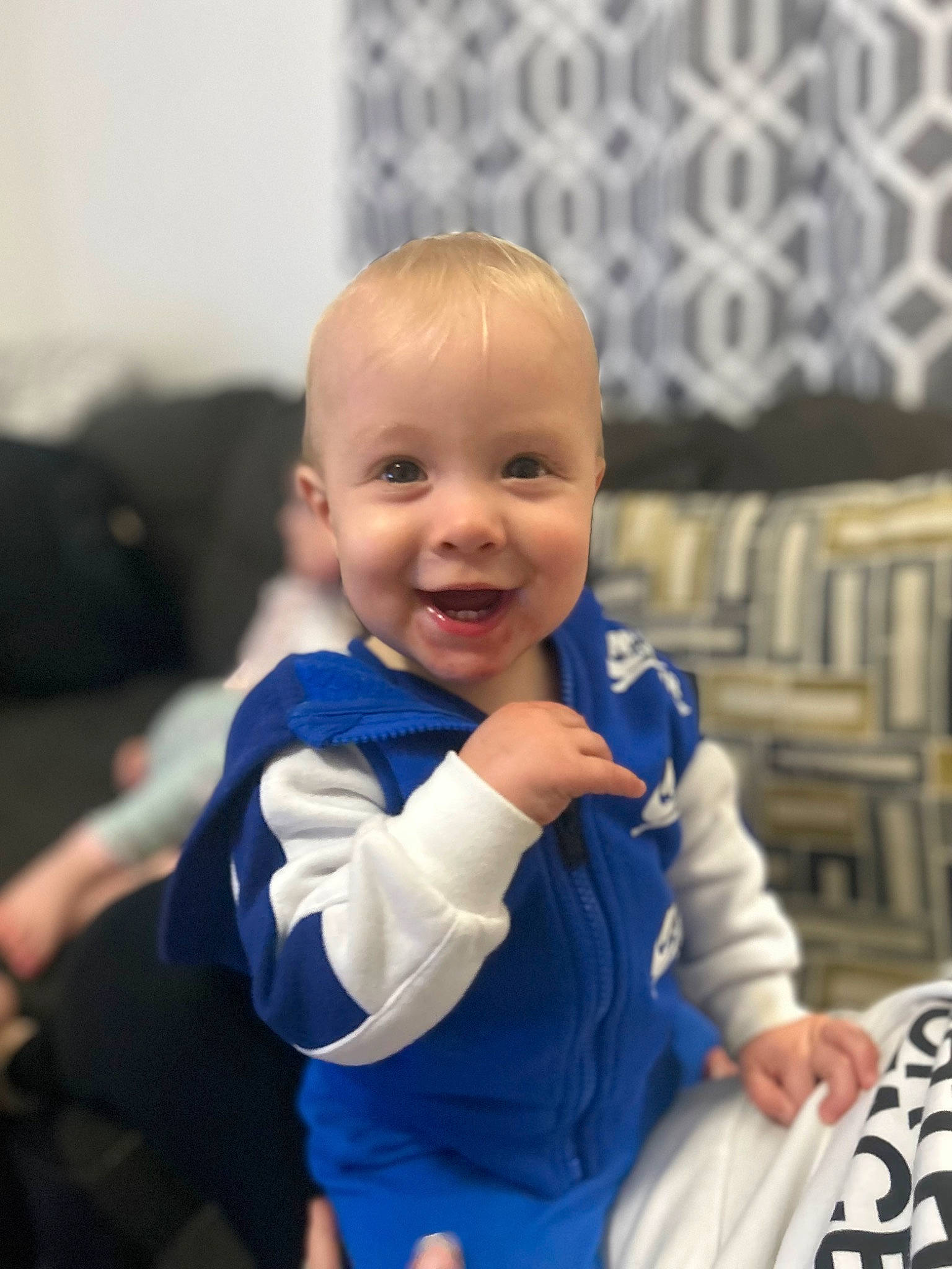 Liam is registered to the contest to win money with this photo: arm, baby, baby_toddler_clothing, cheek, child, comfort, couch, electric_blue, fun, gesture, happy, joy, laugh, leisure, outerwear, person, room, sitting, sleeve, smile