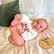 Beckham is registered to the contest to win money with this photo: baby, infant, smiling_baby, blue_eyes, diaper, white_onesie, milestone_disc, wooden_disc, bed, white_bedding, green_pillow, feet, hands, lying_on_back, chubby_legs, cute, portrait, home_interior, soft_light, playful_pose
