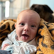Jaxson is registered to the contest to win money with this photo: baby, infant, blanket, leopard_print, tongue_out, face, person, cute, smile, animal, dog, blurred_background, indoor, cozy, soft_texture, clothing, eyes, head, portrait, happy
