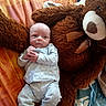 baby, infant, teddy_bear, plush_toy, bed, blanket, clothing, sleepwear, comfort, cute, child, person, soft_toy, resting, indoors, cozy, small, lying_down, stuffed_animal, home
