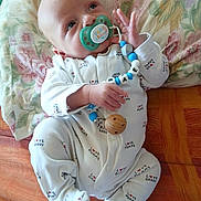 Maë a rejoint le concours — aidez-le/la à gagner de superbes lots ! baby, infant, pacifier, onesie, toy, beads, pillow, floral, fabric, orange, white_clothing, child, cute, lying_down, hand, face, head, footwear, sleepwear, home_interior