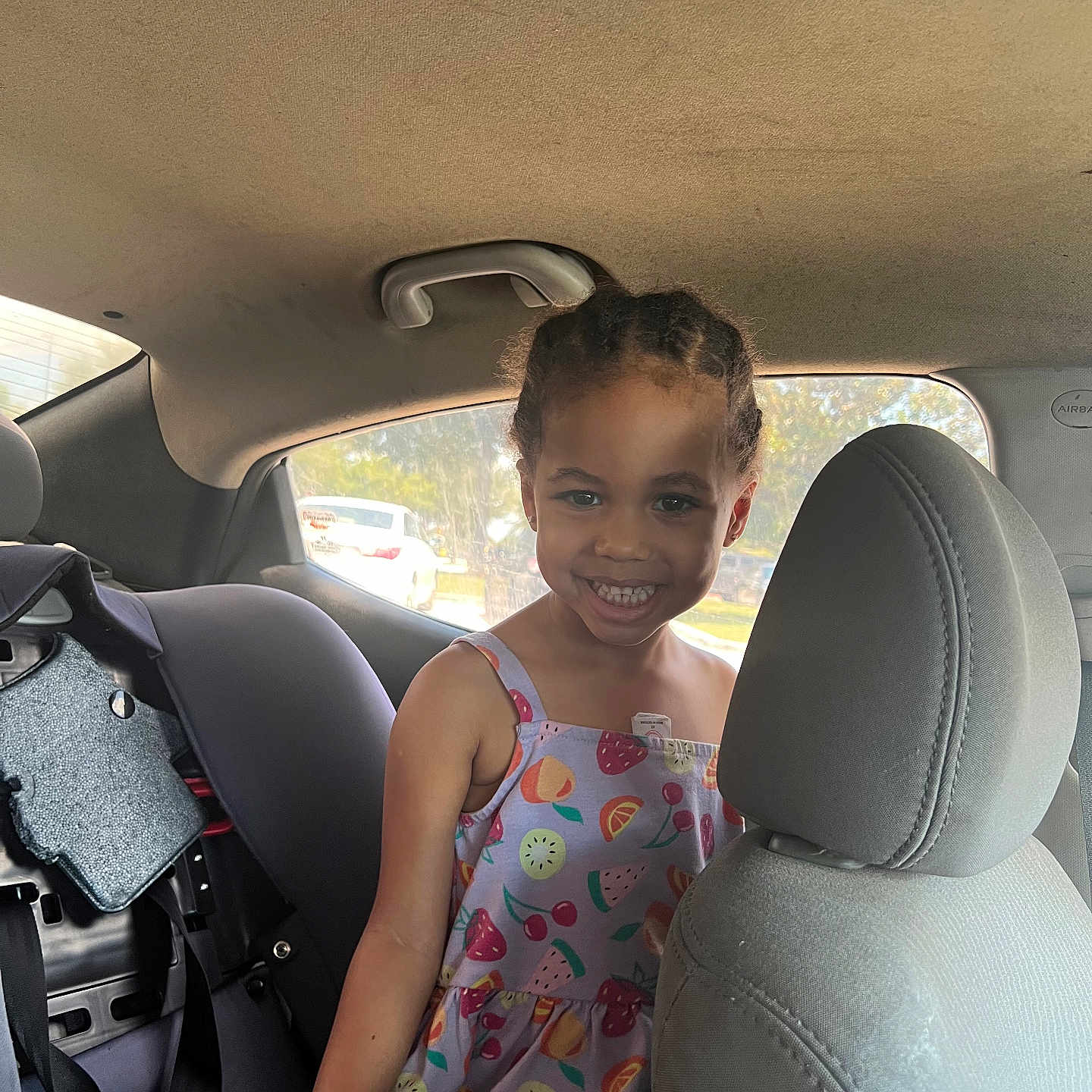 Niome is registered to the contest to win money with this photo: braided_hair, car_interior, car_seat, casual_clothing, child, child_seat, daylight, dress, fruit_pattern, happy, indoor, person, portrait, seat_headrest, seatbelt, smiling, sunlight, vehicle, window, young_child