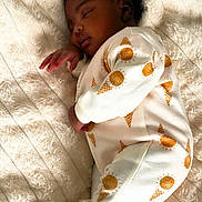 Roxane Adria is registered to the contest to win money with this photo: baby, sleeping, pajamas, blanket, infant, child, soft_texture, cozy, cute, peaceful, patterned_clothing, indoors, resting, warm, comfort, portrait, person, small_hands, curly_hair, sleep