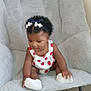 baby, child, sitting, chair, headband, bows, white_socks, strawberry_pattern, curly_hair, indoor, carpet, cute, infant, clothing, footwear, person, furniture, soft_texture, skin, playful