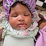 baby, sleeping, pacifier, bonnet, purple, mint_green, clothing, soft_toy, blanket, floral_pattern, face, close_up, infant, cute, resting, indoors, child, peaceful, portrait, cozy