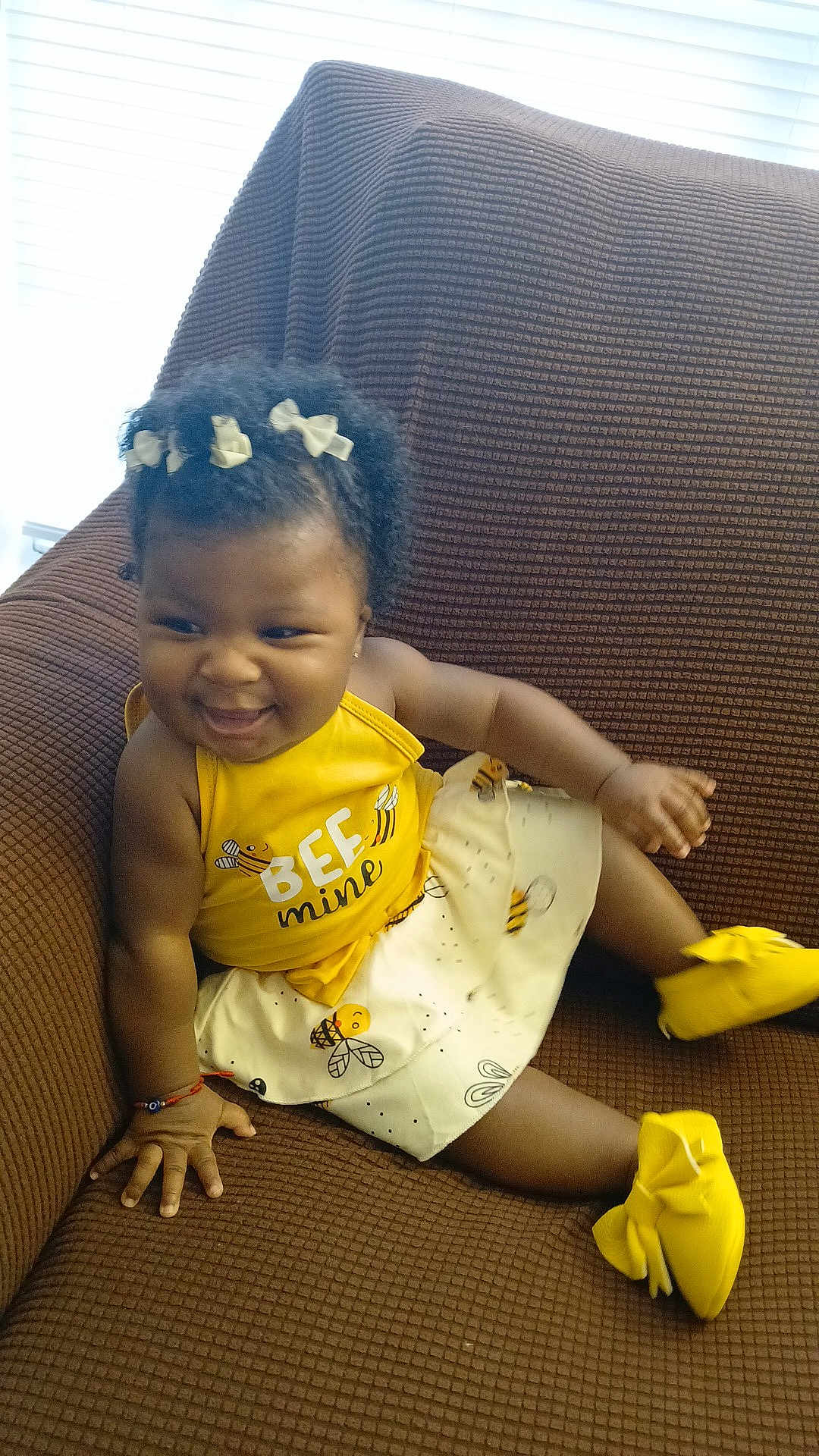 Nanyamka is registered to the contest to win money with this photo: toddler, child, smiling, yellow_clothing, dress, hair_bows, curly_hair, sitting, couch, brown_couch, happy, indoors, footwear, baby, person, cute, playful, fashion, accessory, portrait