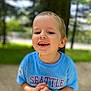 child, boy, smiling, blue_shirt, outdoor, tree, grass, nature, happy, portrait, casual_clothing, short_hair, daylight, young, person, face, background_blur, hands, standing, toddler