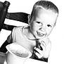 child, toddler, smile, face, short_hair, sitting, table, chair, food_container, snack, black_and_white, portrait, happy, cute, person, indoor, young_child, expression, casual_clothing, closeup