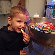 Logan participe au concours pour gagner de l'argent avec cette photo : child, boy, face_paint, candy, snack, bowl, table, indoor, smile, happy, food, sweet, kitchen, plastic_bottle, cup, toy, clothing, short_hair, person, casual