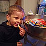 child, boy, face_paint, candy, snack, bowl, table, indoor, smile, happy, food, sweet, kitchen, plastic_bottle, cup, toy, clothing, short_hair, person, casual