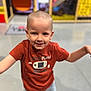 child, boy, smile, tshirt, shorts, indoor, play_area, happy, portrait, casual_clothing, short_hair, young, fun, playful, standing, arms_outstretched, colorful_background, floor, person, kid