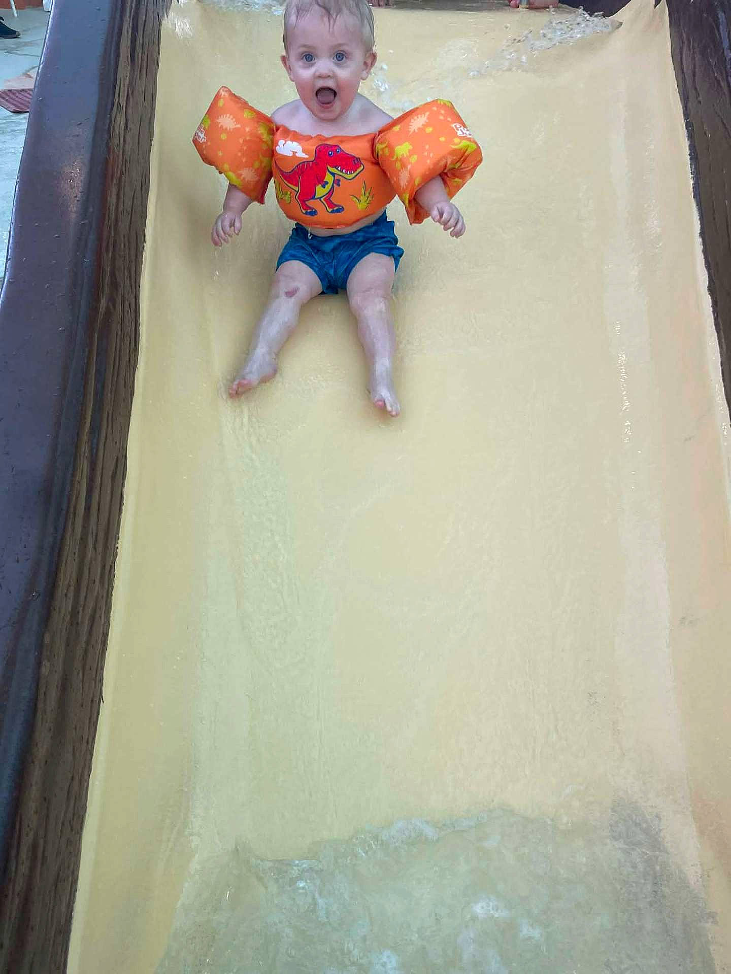 Kaisen is registered to the contest to win money with this photo: child, dinosaur, excitement, floaties, fun, joy, orange, outdoor, person, play, pool, safety, slide, splash, summer, swimwear, toddler, water, water_slide, waterpark