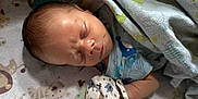 Theo is registered to the contest to win money with this photo: newborn, baby, sleeping, blanket, mitten, infant, face, bed, patterned_blanket, peaceful, closeup, person, cute, soft_lighting, human, resting, indoors, child, clothing, toddler